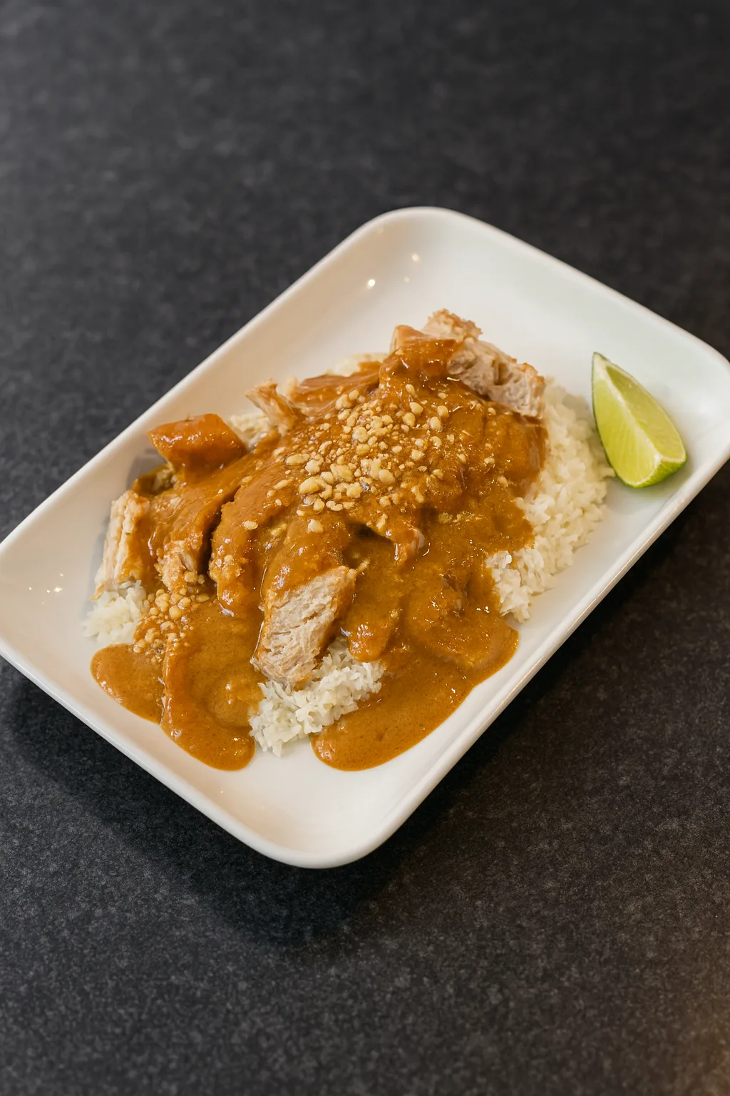 Instant Pot peanut lime satay chicken served over white rice with peanut sauce, crushed peanuts, and lime wedge on a dark countertop