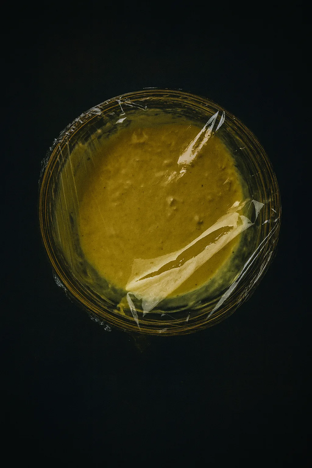 Honey mustard sauce in a bowl covered with plastic wrap